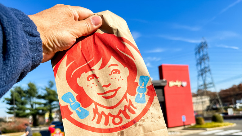 Hand holding Wendy's bag in front of franchise location