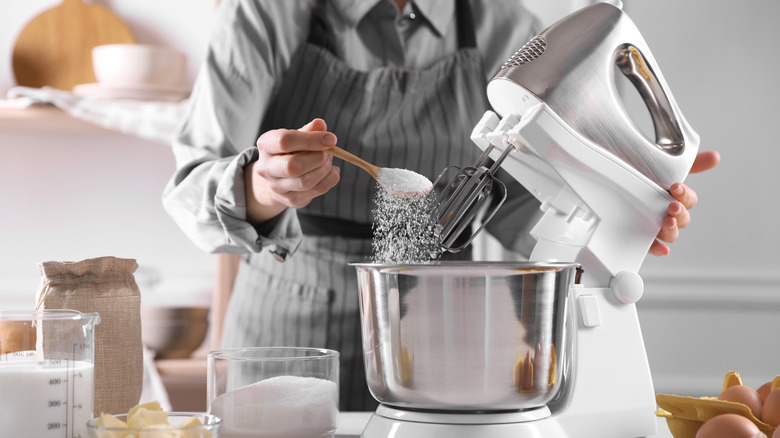 A woman adding ingredients to the bowl on a stand mixer