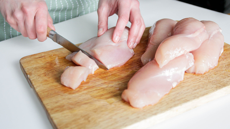 A woman slicing raw chicken breasts on a cutting board.