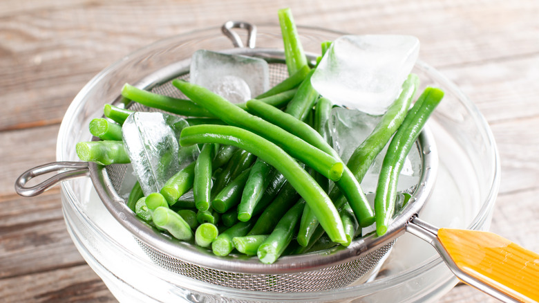 green beans in a colander and bowl full of ice water