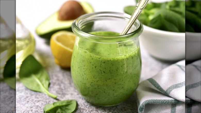 jar of green goddess dressing with sliced lemon and avocado blurred in the background