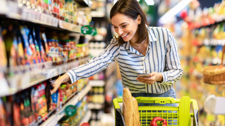 woman grocery shopping while holding phone