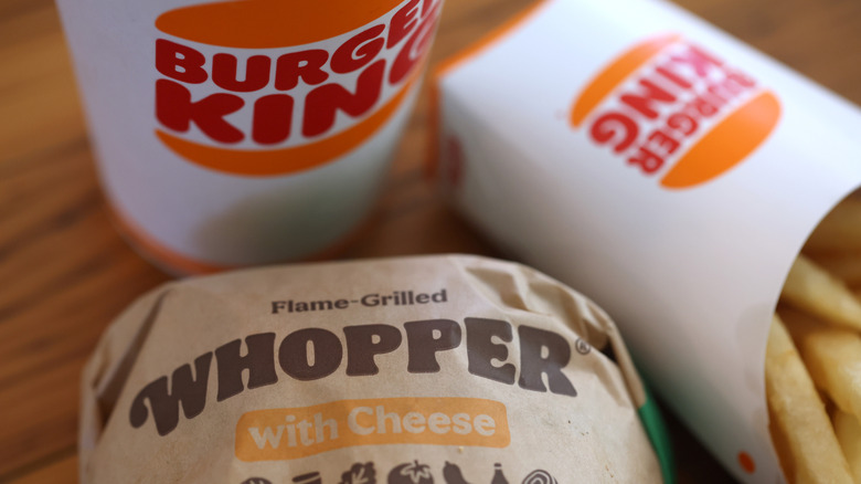 Flame grilled Whopper with cheese in wrapper with soda cup and fries