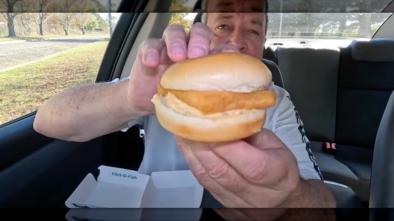 Man sitting in car, holding a Filet-O-Fish with Big Mac sauce up to the camera