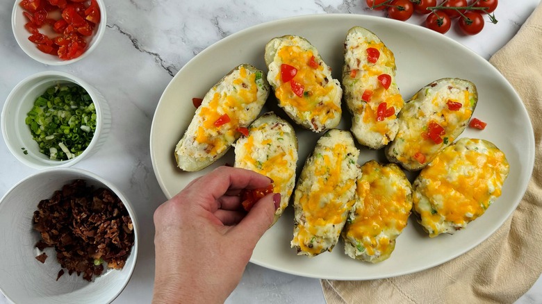 hand putting tomatoes on potatoes