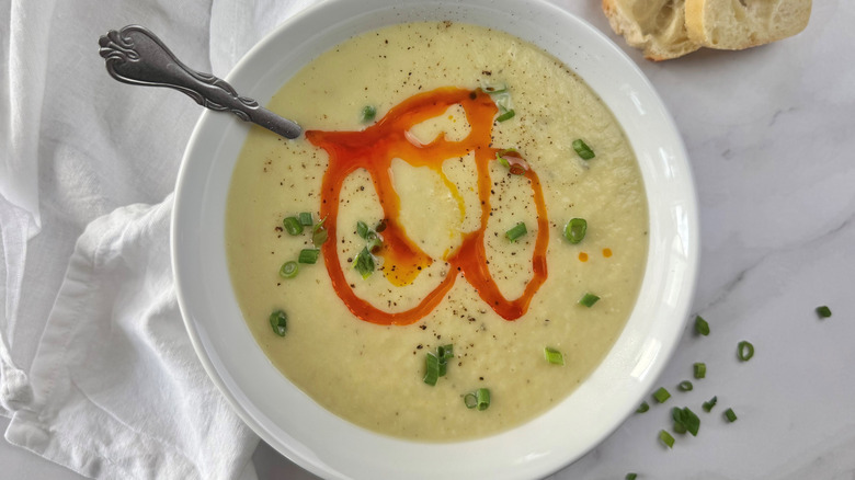 Cream soup in a white bowl topped with green onions and red oil