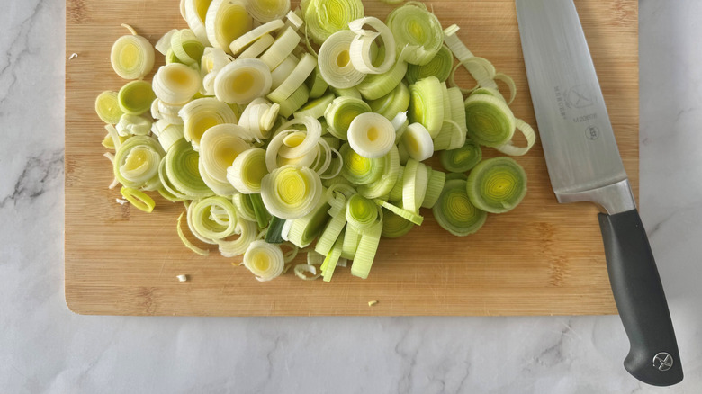 Chopped leeks on a wooden board with a knife