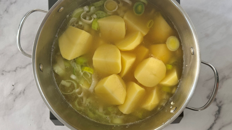 Chopped leeks and potatoes in a metal pot full of liquid