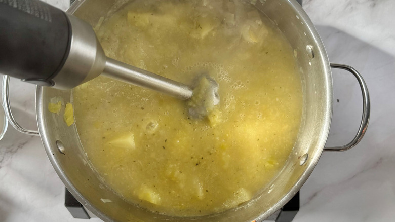 Immersion blender in a metal pot full of lumpy yellow liquid