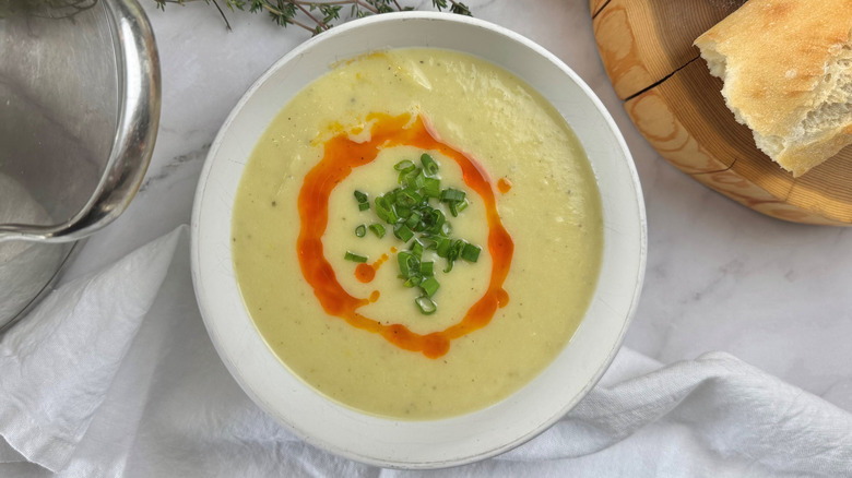 Cream soup in a white bowl topped with green onions and red oil