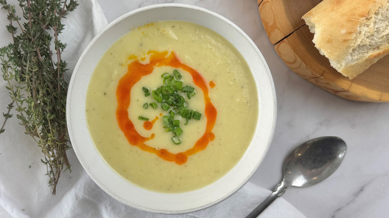 Cream soup in a white bowl topped with green onions and red oil