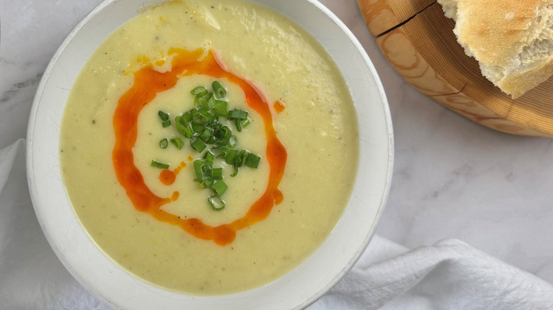 Cream soup in a white bowl topped with green onions and red oil