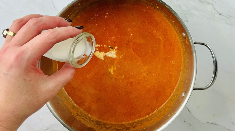 hand pouring cream into pureed tomatoes