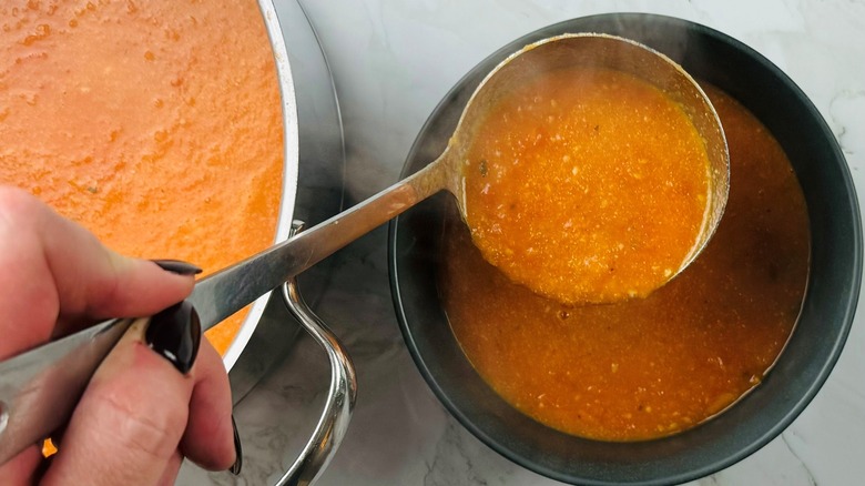 hand holding ladle of tomato soup