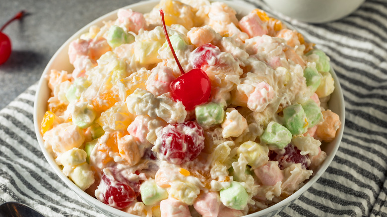 A bowl of ambrosia salad with a maraschino cherry on top