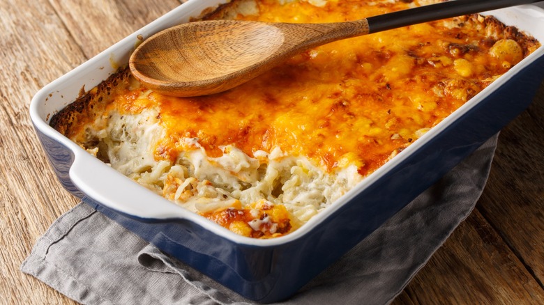 A dish of hash brown casserole with a wooden spoon on top