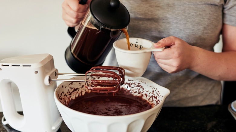 Person pouring a cup of coffee standing over a chocolate batter in a mixer