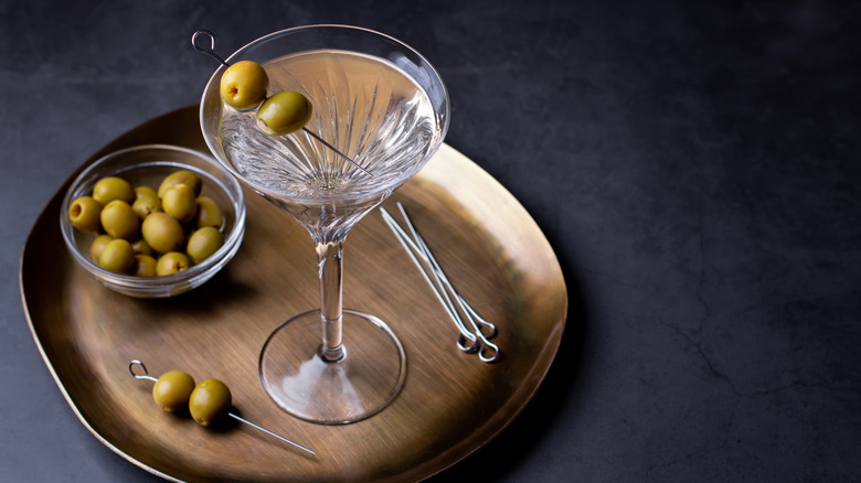 Dirty martini on a wooden plate with a bowl of green olives