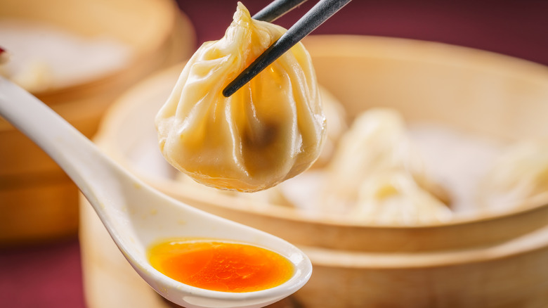 Soup dumpling held over spoon with chopsticks