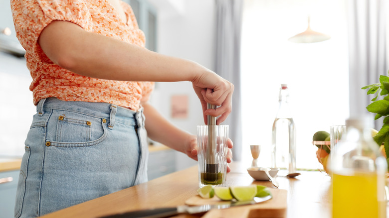 Person muddling a drink at wood counter.