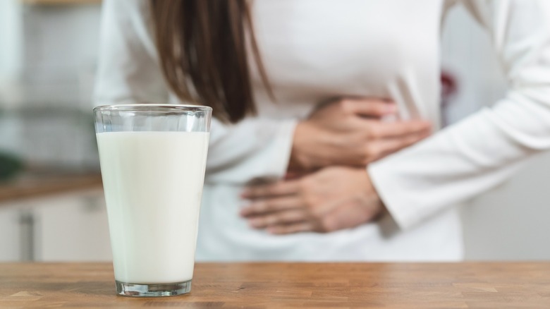 Glass of milk on wood table in front of person holding stomach