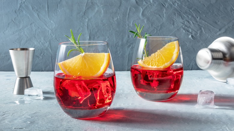 Two red cocktails over ice with orange slices. 