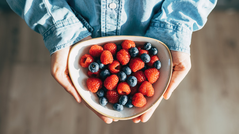 Hands hold a bowl of raspberries and blueberries