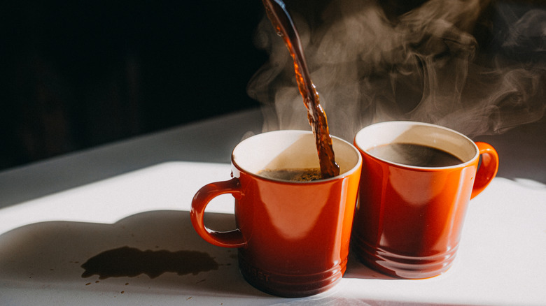 Coffee being poured into two mugs.