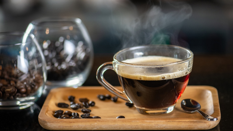 Hot coffee in a glass mug on a wooden tray with coffee beans