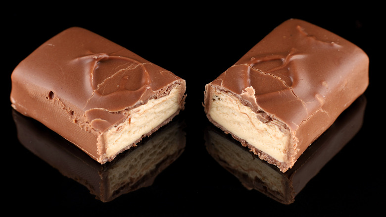 Milky Way bar cut in half displaying nougat inside on dark, reflective background