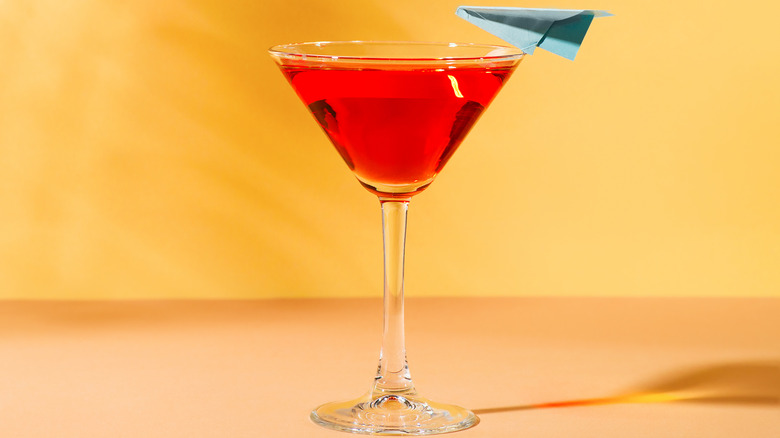 martini glass filled with a red drink and garnished with a light blue paper airplane