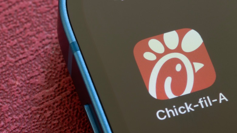 A close-up of the Chick-fil-A app icon is displayed on a phone in a blue case on a red background.