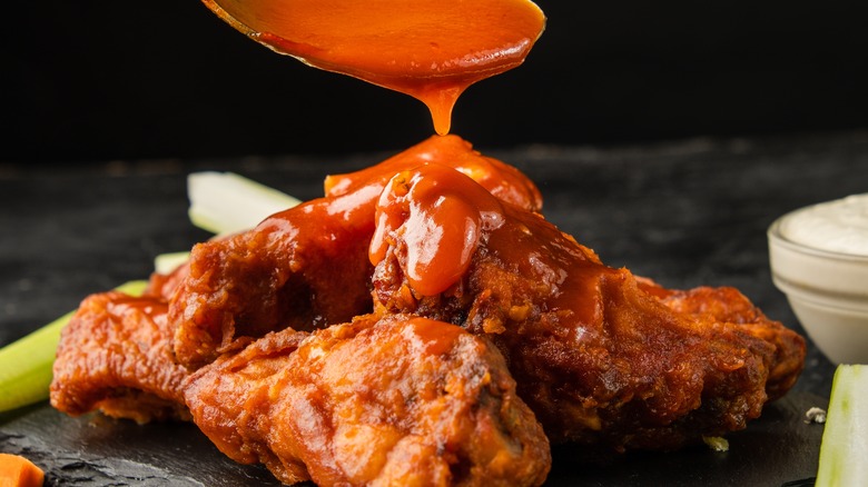 spoon drizzling buffalo sauce onto fried chicken wings