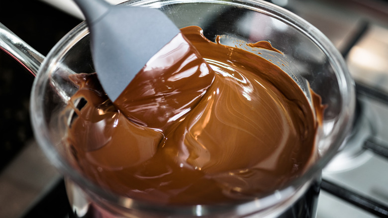 Melted chocolate in a glass bowl with a spoon on a stovetop.