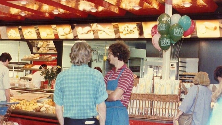 John Mackey, in a blue apron, stands in the middle of a busy Whole Foods Market store