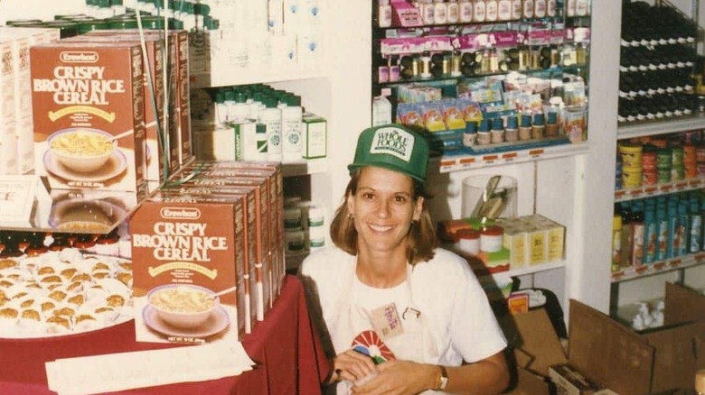 A woman wearing a Whole Foods cap sits in front of a display of crispy brown rice cereal