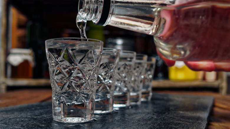 Pouring vodka into a row of shot glasses