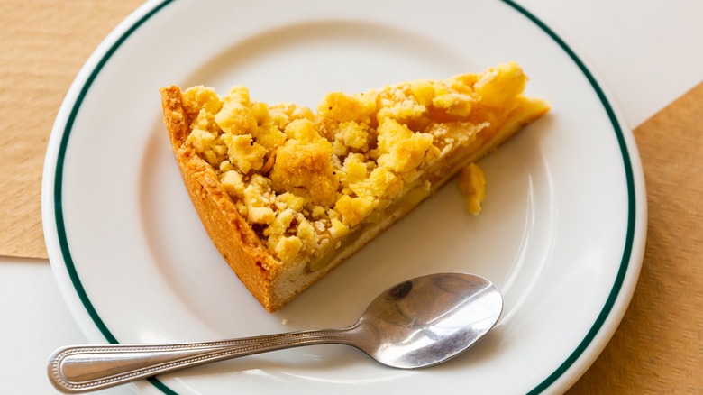 A wedge of Dutch apple pie on white dessert plate with spoon