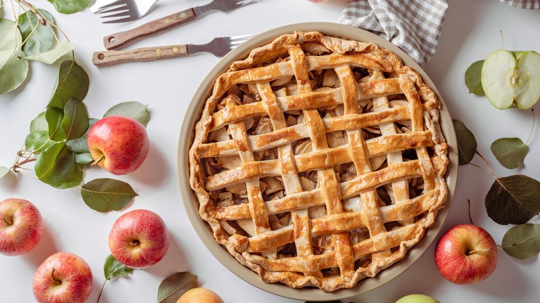 A latticed apple pie sits atop a white surface with gray gingham napkins.