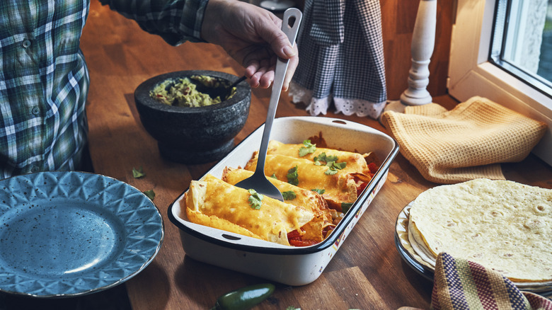 man using a spatula to serve an enchilada from a baking dish