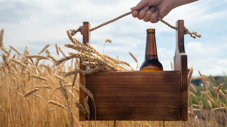person holding a wooden basket with a bottle of beer