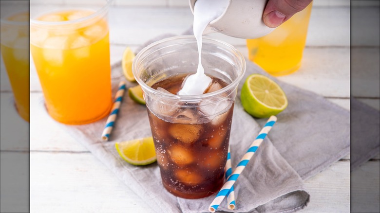 pouring sweet cream into a clear plastic cup of cola