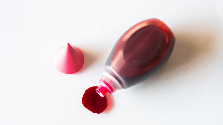 A bottle of red food coloring is spilled on a white surface