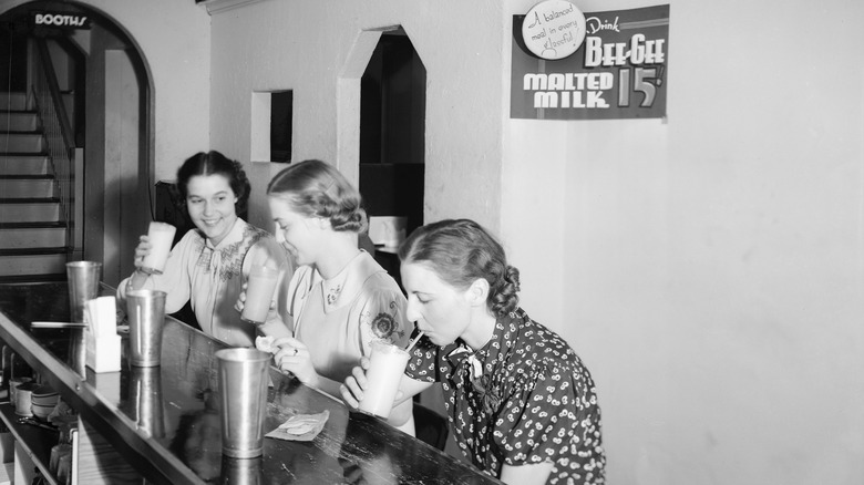 Three women drinking malted shakes at a soda fountain