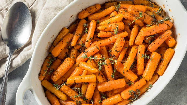 Roasted Baby Carrots with herbs on a white dish with a spoon next to it on a fabric napkin.