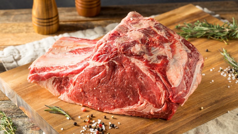 Raw prime rib roast on wood cutting board with rosemary, salt, and pepper