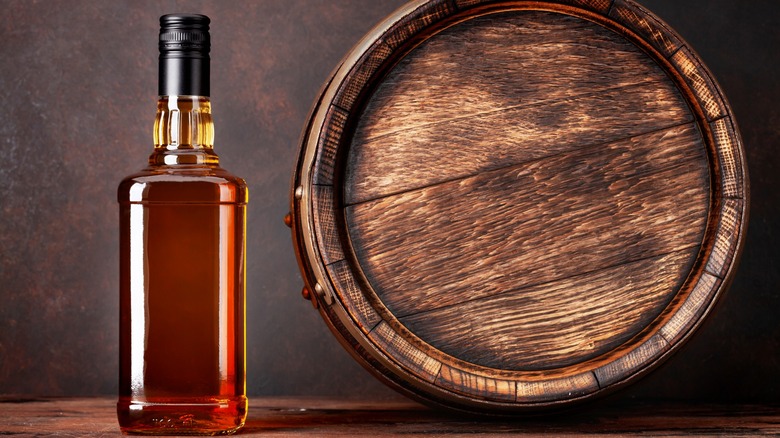 Upright whiskey bottle next to wooden barrel