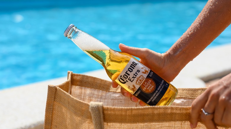 taking a bottle of Corona Extra out of a burlap beach bag