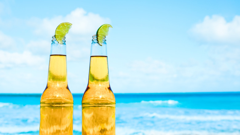 two unlabeled bottles of Mexican lager with limes in them with the ocean in the background