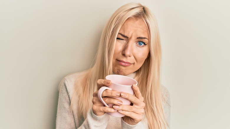 Woman holding coffee cup with skepticism